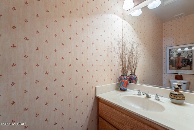 bathroom featuring toilet, wallpapered walls, vanity, and visible vents