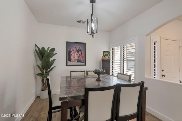 dining space with arched walkways, visible vents, wood finished floors, and baseboards