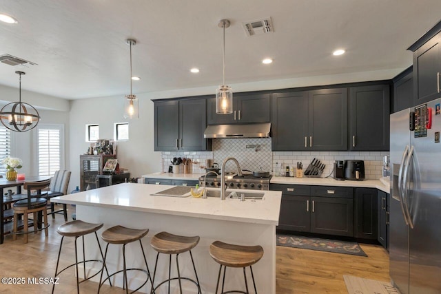 kitchen featuring stainless steel fridge, visible vents, light wood-style flooring, and under cabinet range hood