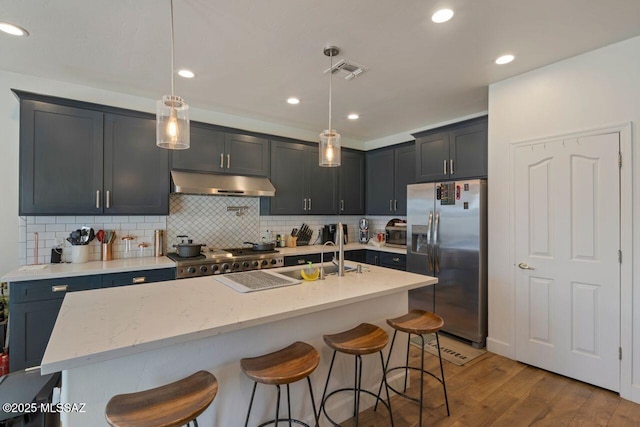 kitchen featuring light stone countertops, a sink, under cabinet range hood, stainless steel fridge, and visible vents