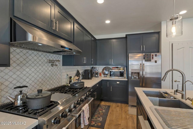 kitchen featuring a sink, appliances with stainless steel finishes, light countertops, under cabinet range hood, and backsplash
