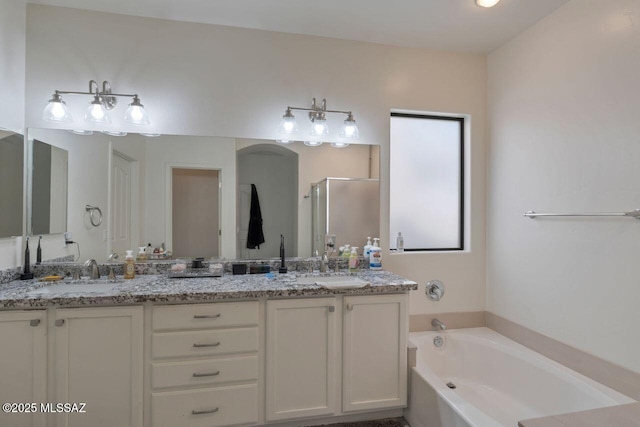 bathroom featuring double vanity, a garden tub, a shower stall, and a sink