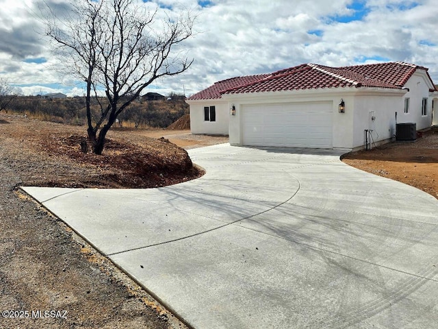 view of side of property featuring a tiled roof, central air condition unit, stucco siding, an attached garage, and concrete driveway