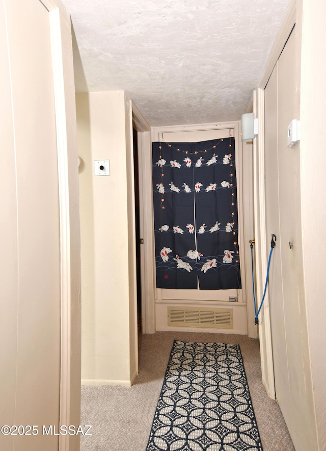hallway with a textured ceiling, visible vents, carpet flooring, and baseboards