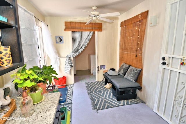 sitting room featuring ceiling fan and wooden walls