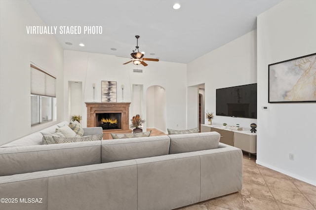 living area featuring ceiling fan, a lit fireplace, visible vents, a high ceiling, and baseboards