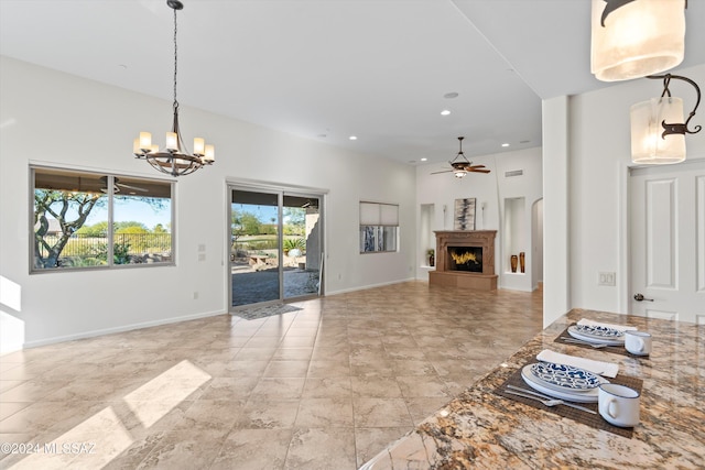 unfurnished living room with a lit fireplace, ceiling fan with notable chandelier, baseboards, and recessed lighting