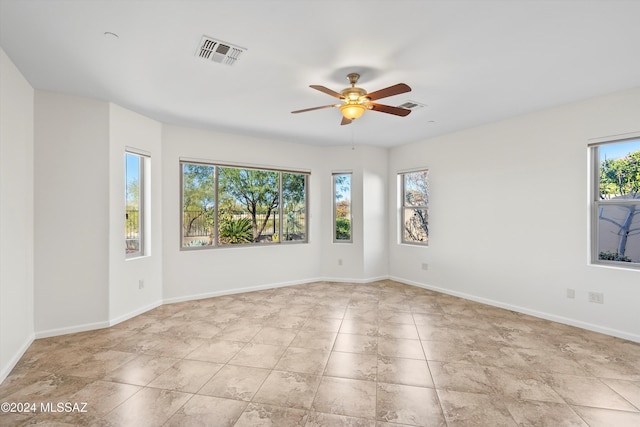 tiled empty room with baseboards, a ceiling fan, and visible vents