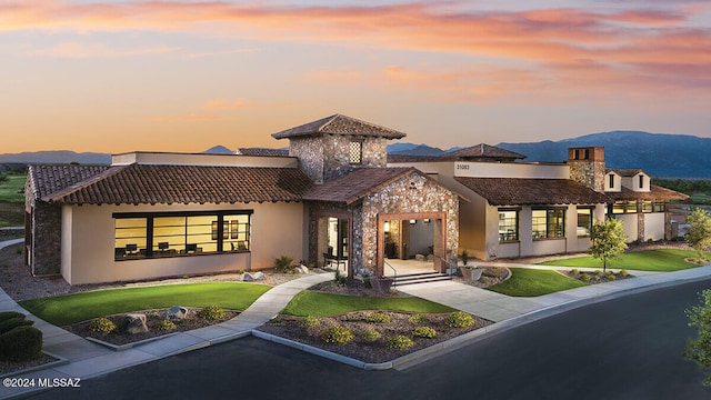 back of house with a tiled roof, a mountain view, a lawn, and stucco siding