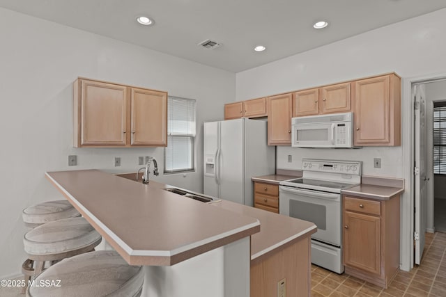kitchen with white appliances, light brown cabinets, a sink, and a kitchen bar