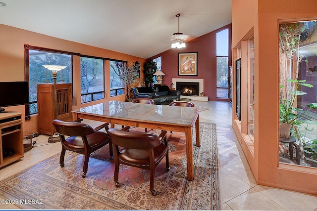 dining space featuring a warm lit fireplace, light tile patterned floors, a ceiling fan, and vaulted ceiling