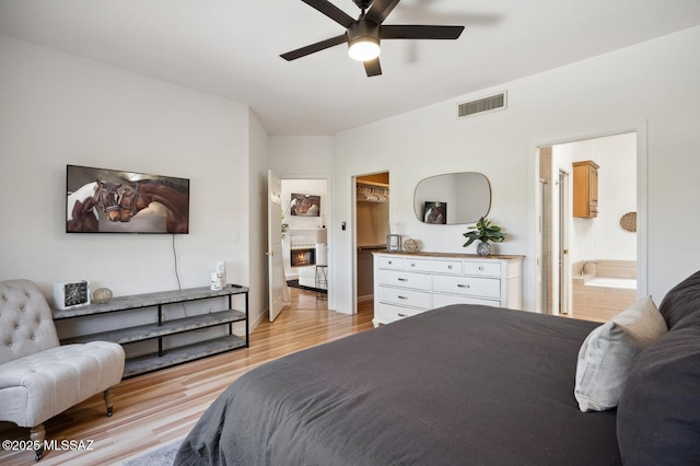 bedroom with a spacious closet, ensuite bath, light wood-style floors, visible vents, and ceiling fan