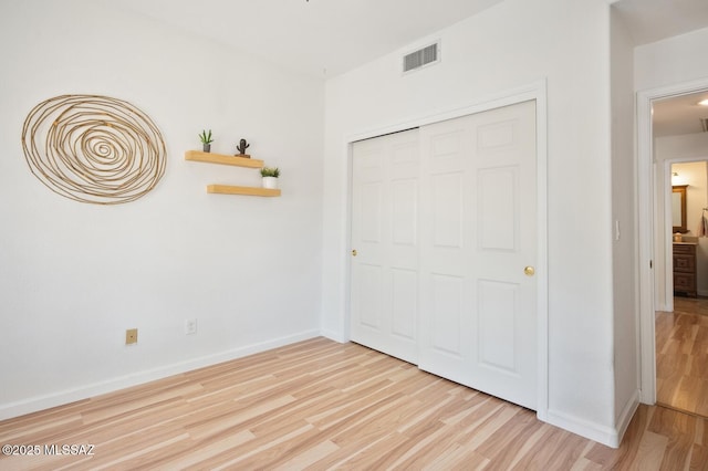 unfurnished bedroom with wood finished floors, baseboards, a closet, and visible vents