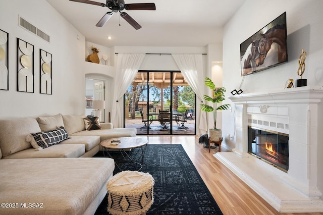 living area featuring visible vents, arched walkways, ceiling fan, a fireplace, and wood finished floors