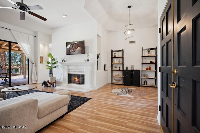 living room featuring a glass covered fireplace, baseboards, a ceiling fan, visible vents, and light wood finished floors