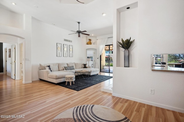 living room with ceiling fan, arched walkways, visible vents, wood finished floors, and baseboards