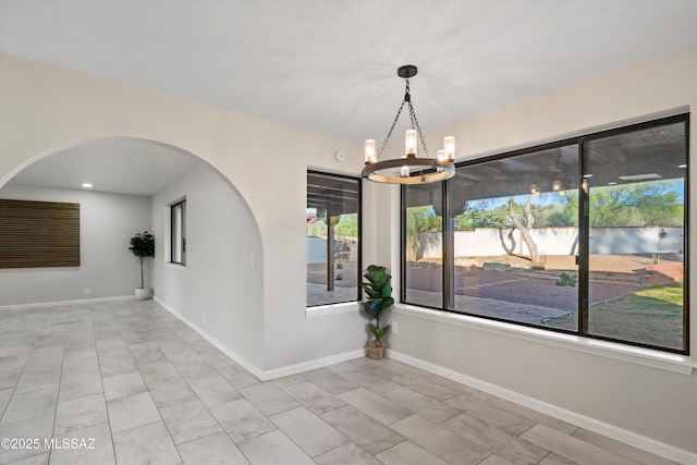 tiled empty room with arched walkways, baseboards, and a chandelier