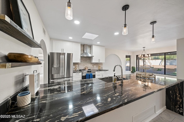 kitchen featuring appliances with stainless steel finishes, a sink, wall chimney exhaust hood, tasteful backsplash, and visible vents