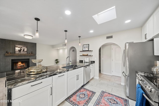 kitchen with a sink, arched walkways, dark stone countertops, stainless steel appliances, and visible vents