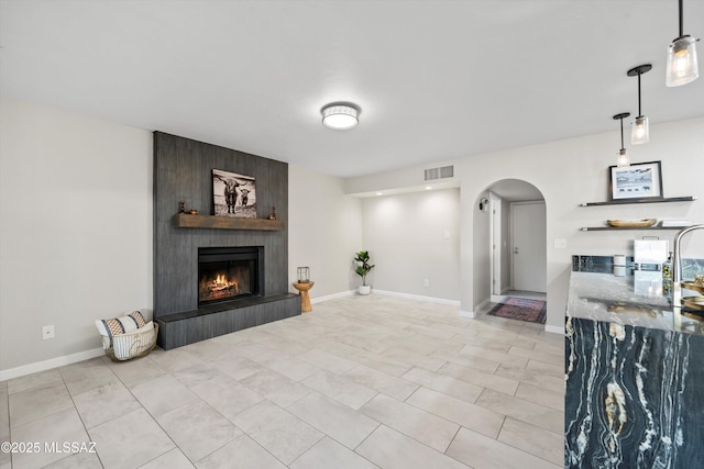 unfurnished living room with light tile patterned flooring, arched walkways, a large fireplace, baseboards, and visible vents