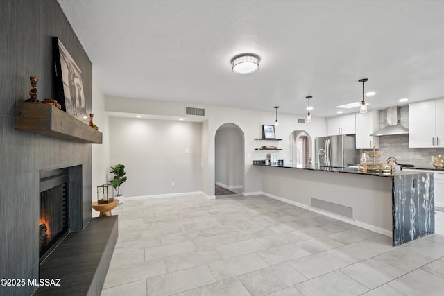 kitchen featuring stainless steel fridge with ice dispenser, arched walkways, wall chimney exhaust hood, and visible vents