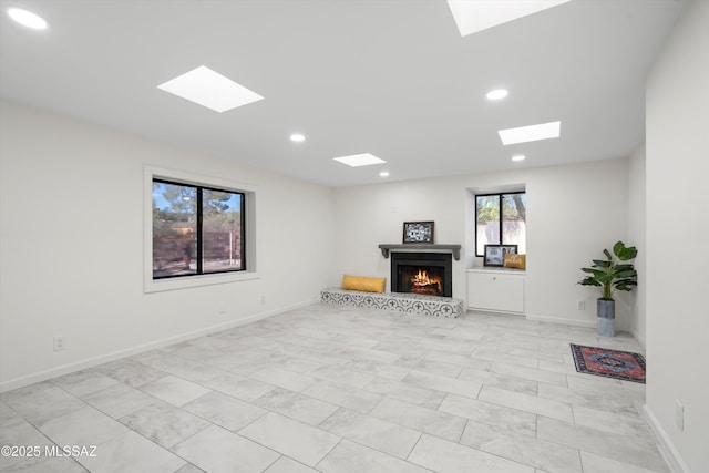 unfurnished living room with recessed lighting, a skylight, a lit fireplace, and baseboards