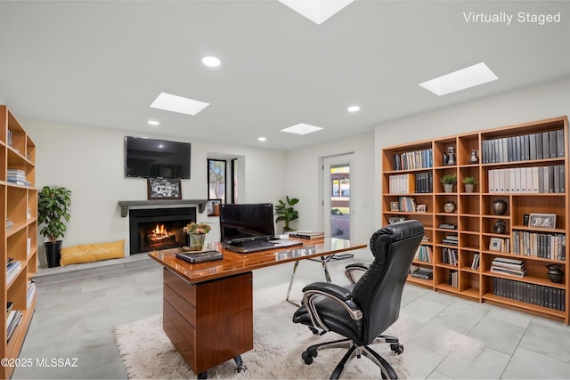 home office featuring a skylight, recessed lighting, and a warm lit fireplace
