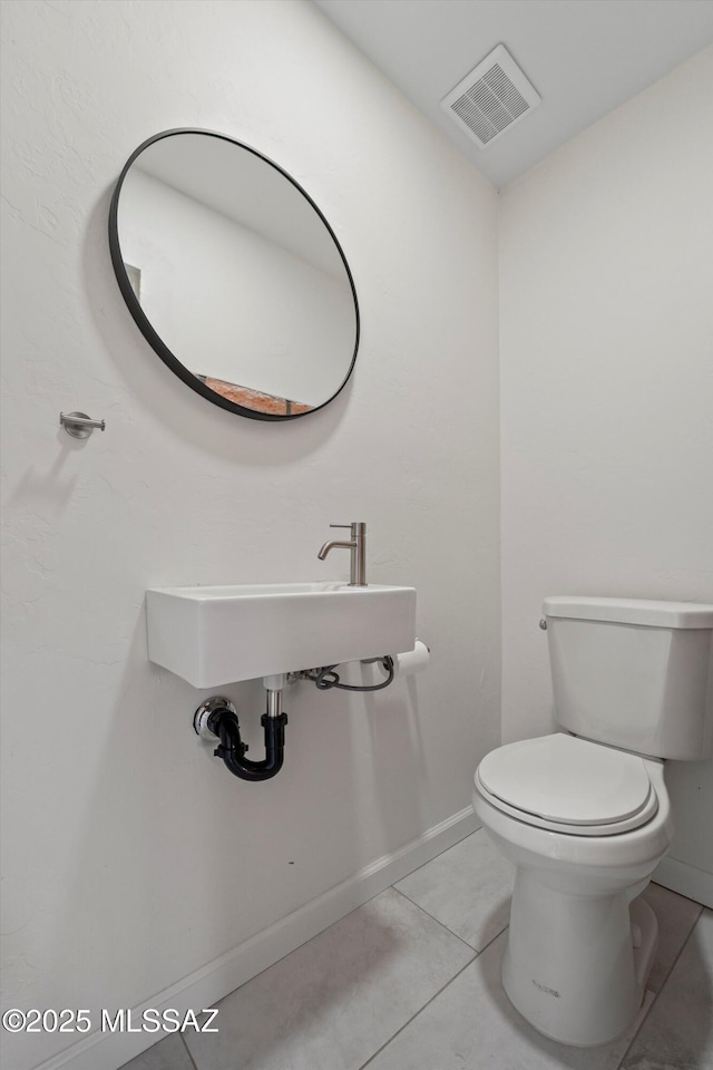 half bath with visible vents, toilet, baseboards, tile patterned floors, and a sink