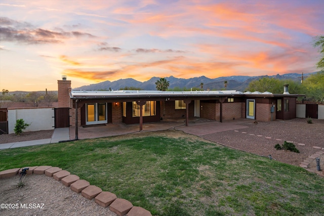 back of house at dusk with a yard, a mountain view, an attached carport, and brick siding