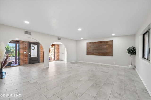 unfurnished living room with arched walkways, recessed lighting, and visible vents