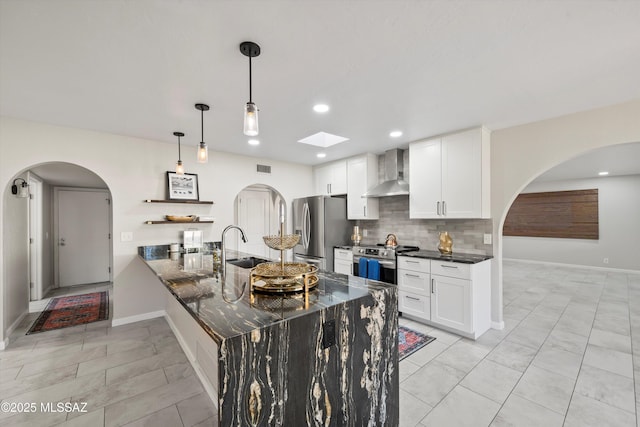 kitchen with wall chimney range hood, decorative backsplash, appliances with stainless steel finishes, white cabinets, and a peninsula