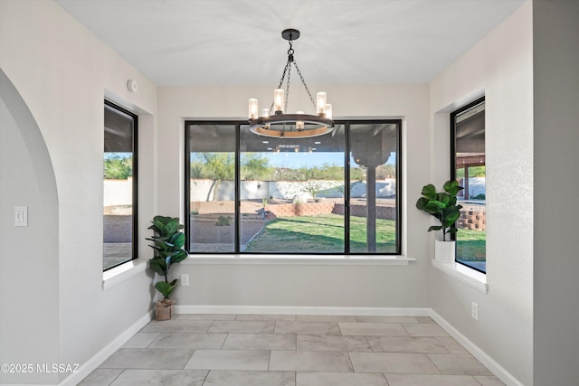 unfurnished dining area featuring baseboards, a notable chandelier, and a wealth of natural light