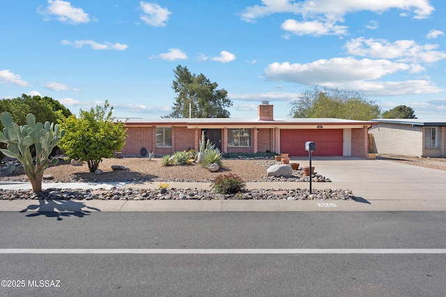 single story home featuring an attached garage, a chimney, driveway, and brick siding