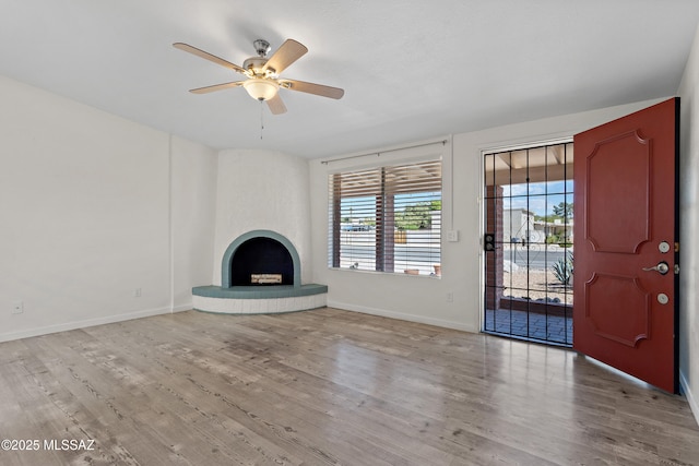 unfurnished living room featuring wood finished floors, baseboards, a ceiling fan, and a fireplace with raised hearth
