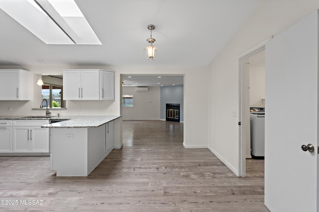 kitchen with washer / clothes dryer, white cabinets, a sink, light wood-type flooring, and a peninsula