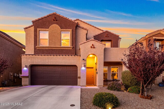 mediterranean / spanish-style house featuring a tiled roof, a garage, stucco siding, and concrete driveway