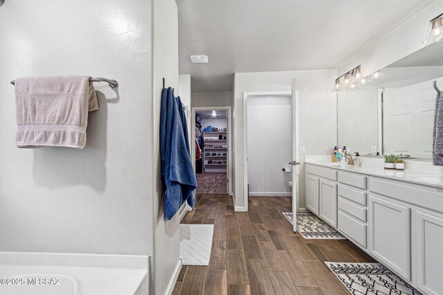 full bath featuring toilet, wood finished floors, a sink, a walk in closet, and double vanity