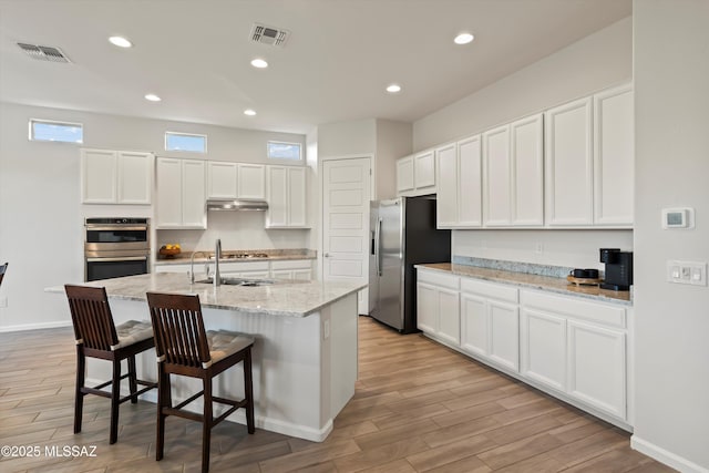 7797 S Indian Wheat Way, Tucson, AZ 85747 - kitchen with appliances with stainless steel finishes, light wood-type flooring, under cabinet range hood, white cabinetry, and an island with sink