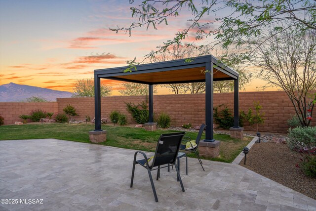 patio terrace at dusk with a fenced backyard, a gazebo, a mountain view, and a yard