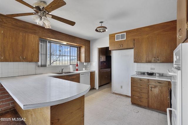 kitchen featuring visible vents, white dishwasher, light countertops, a peninsula, and brown cabinetry
