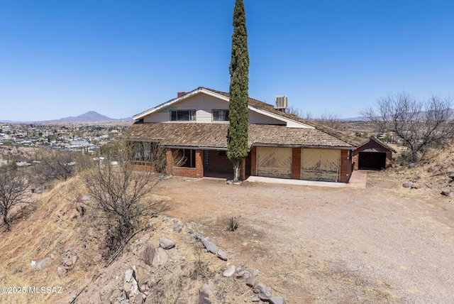 view of front facade featuring a mountain view, driveway, brick siding, central AC, and a garage