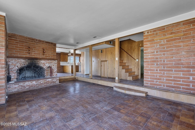 unfurnished living room with visible vents, stairway, and a brick fireplace