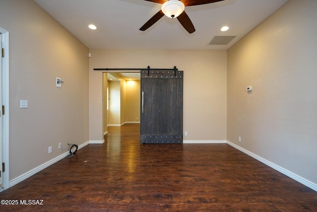 spare room with baseboards, a ceiling fan, a barn door, visible vents, and wood finished floors