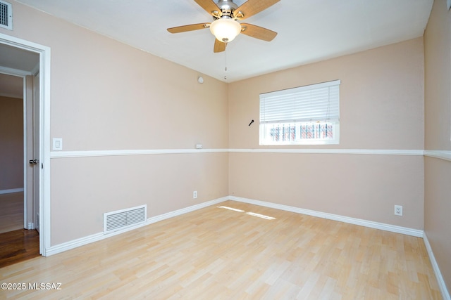 spare room featuring wood finished floors, ceiling fan, baseboards, and visible vents