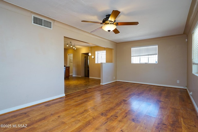 empty room featuring wood finished floors, ceiling fan, baseboards, and visible vents
