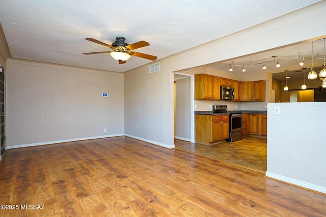 kitchen featuring a ceiling fan, dark countertops, brown cabinetry, appliances with stainless steel finishes, and wood finished floors