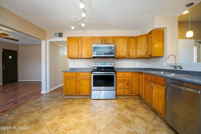 kitchen with light tile patterned floors, a sink, appliances with stainless steel finishes, dark countertops, and brown cabinets