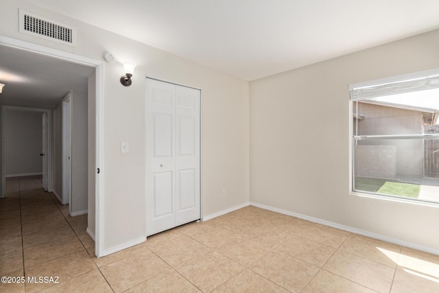 unfurnished bedroom with light tile patterned floors, visible vents, baseboards, and a closet
