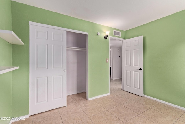 unfurnished bedroom with light tile patterned flooring, visible vents, a closet, and baseboards