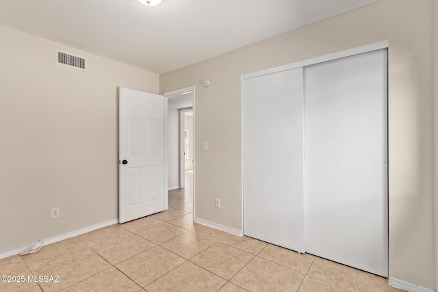 unfurnished bedroom with light tile patterned floors, a closet, visible vents, and baseboards